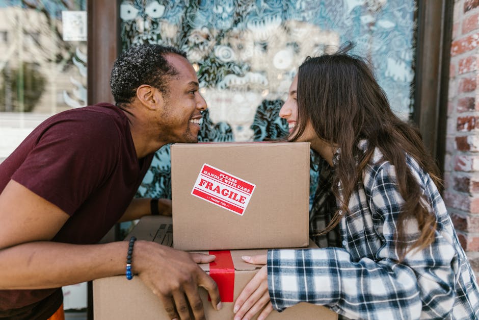 A man and woman are engaged in a home relocation process outside a building, with both individuals leaning close to each other and smiling. The man, wearing a maroon T-shirt and a beaded bracelet, is 